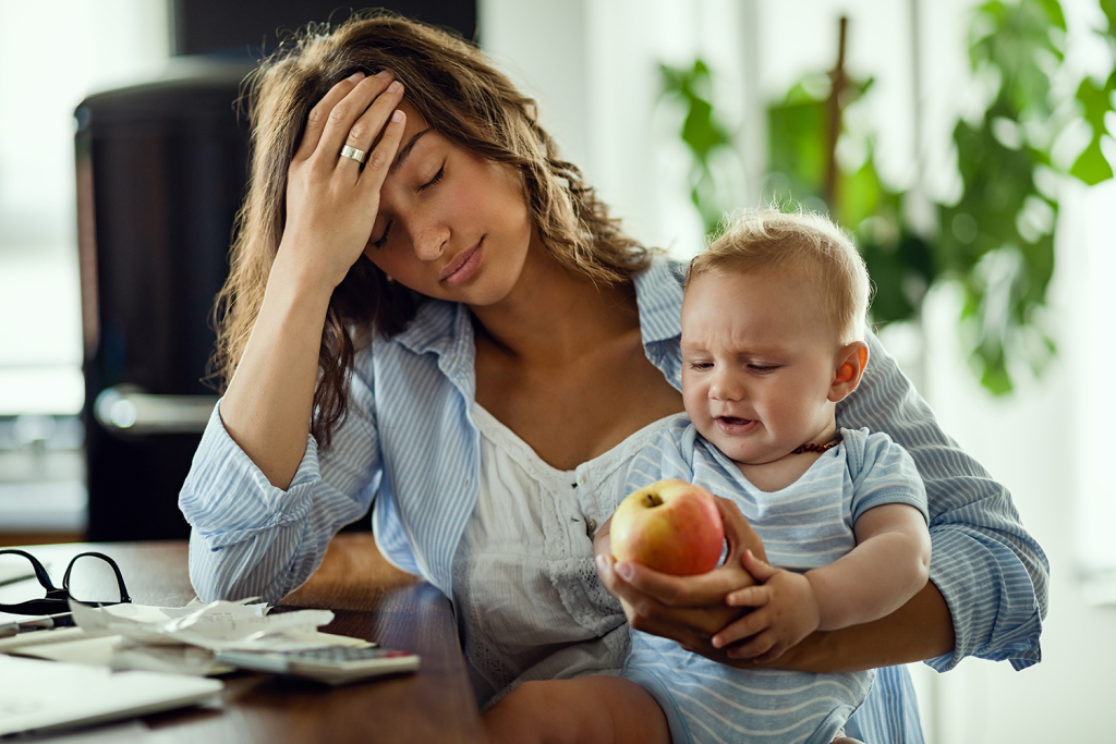 Young mother holds baby while looking stressed, creating a budget when between jobs