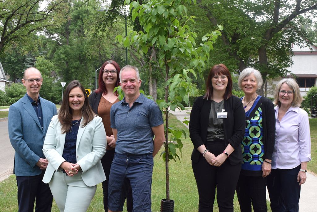 Smiling team members from ACU and Trees Winnipeg posing in front a newly planted tree