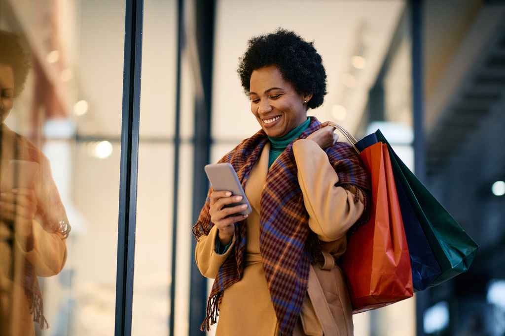 Woman smiling at her phone and holding shopping bags