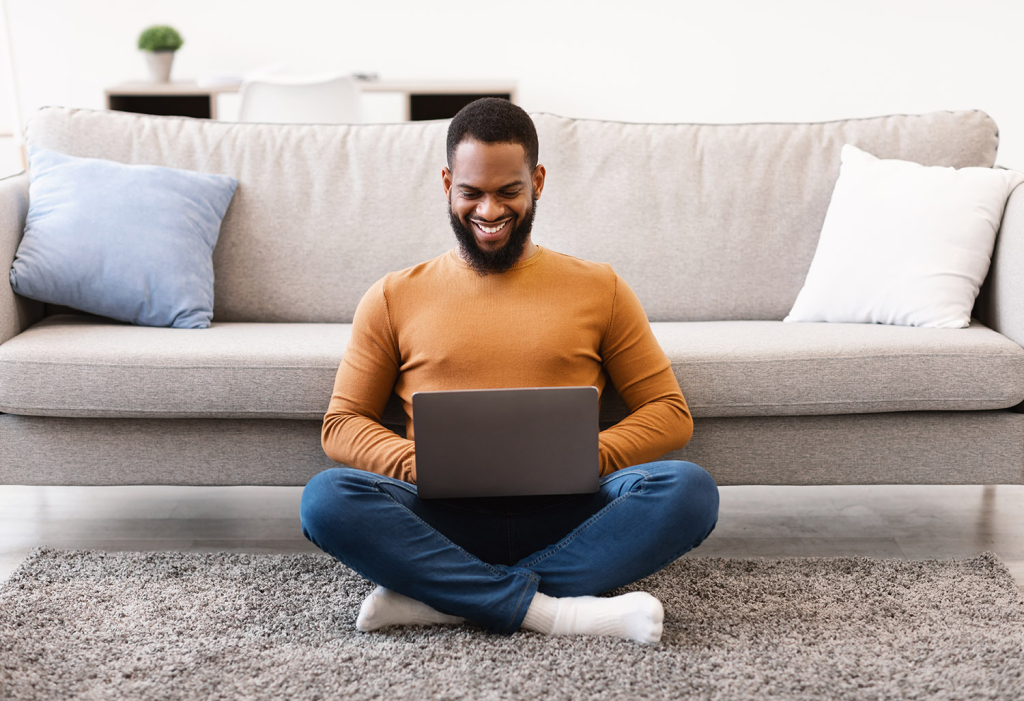 Man suiting on living room floor, smiling at laptop