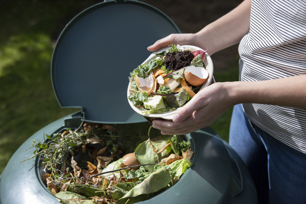 Close up of kitchen scraps being placed in an outdoor compost bin