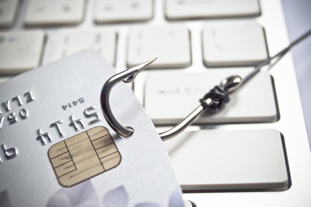 A credit card caught on a fish hook and resting on a keyboard; about to be drawn away