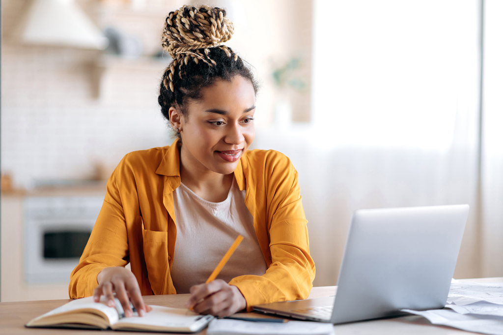 Student in front of a laptop taking notes at home