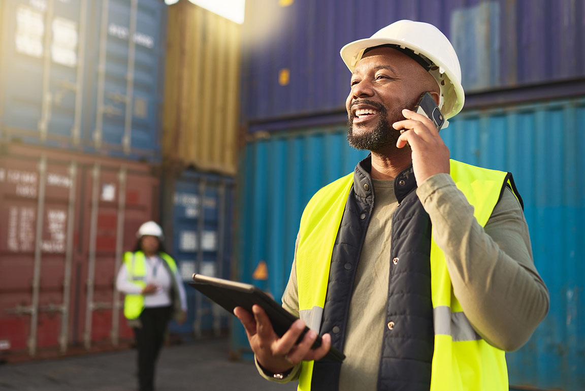 Businessman in freight and transportation holding mobile phone using a tablet to check shipping container inventory, talking with business advisor about business operating line of credit