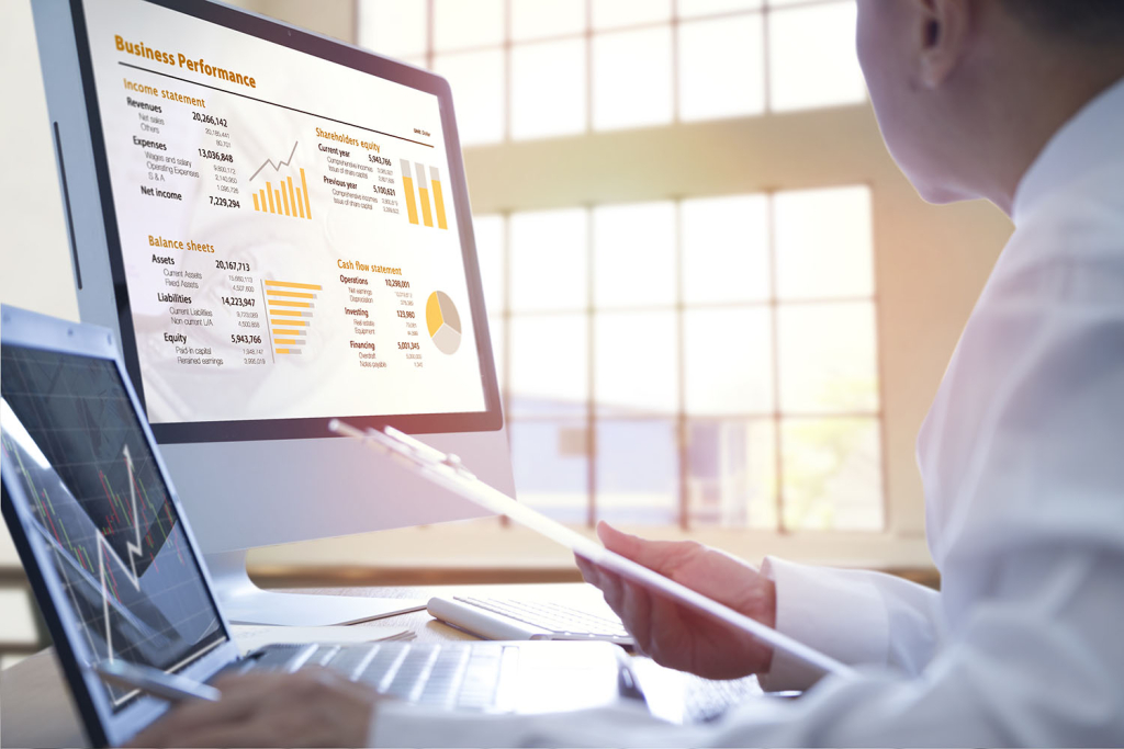 Businessman analyzing on business performance on desktop and notebook computer with orange-gold graphs, income statement, shareholder equity, balance sheets, cash flow statements.