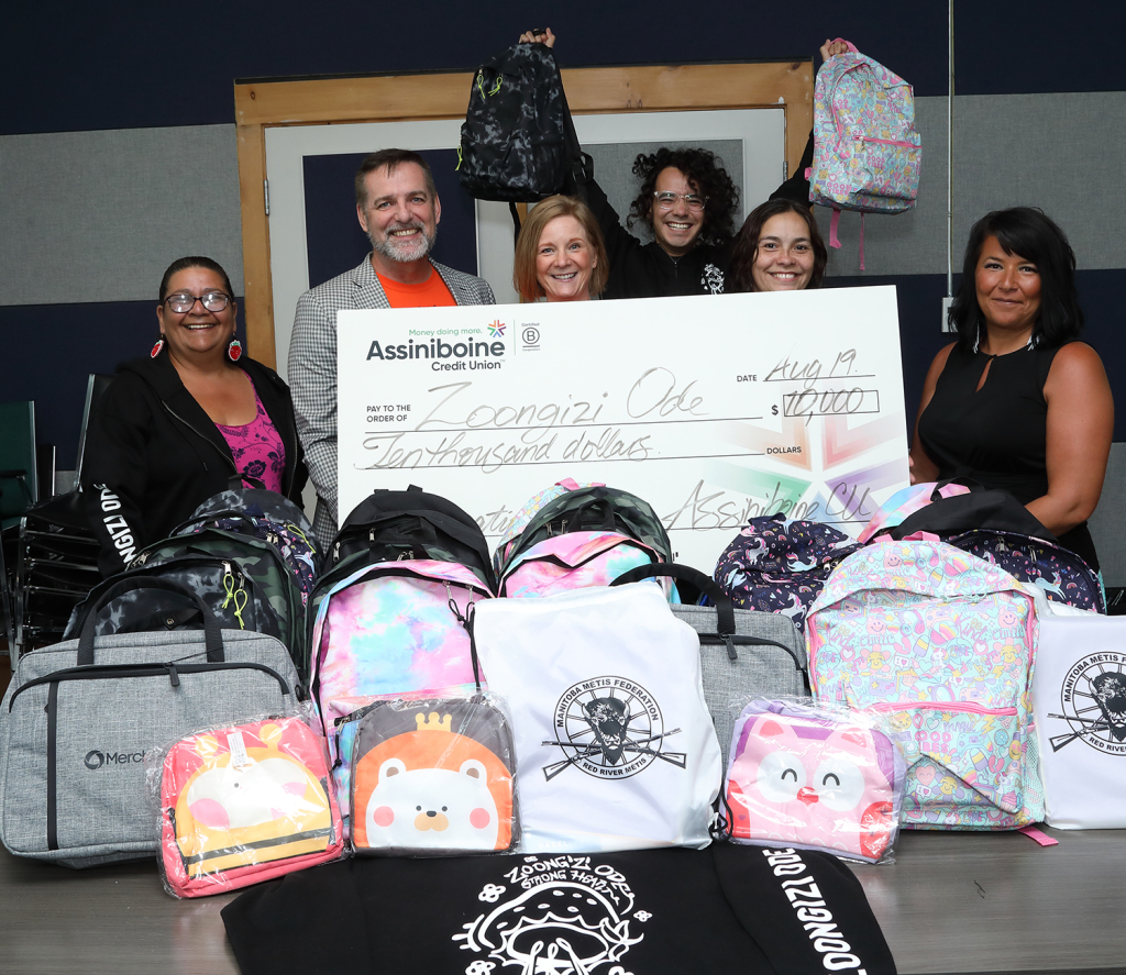 Image of Zoongizi Ode Executive Director, Mary Burton, being presented a cheque for $10,000 by Kim Champion Taylor, Chief People & Brand Officer, Brendan Reimer, Strategic Partner, Values-Based Banking, and Indigenous Leadership Circle Members, Kimberley Mercer and Lisa Delorme Meiler. Michael Redhead Champagne holds two of 20 backpacks donated by the Indigenous Leadership Circle.