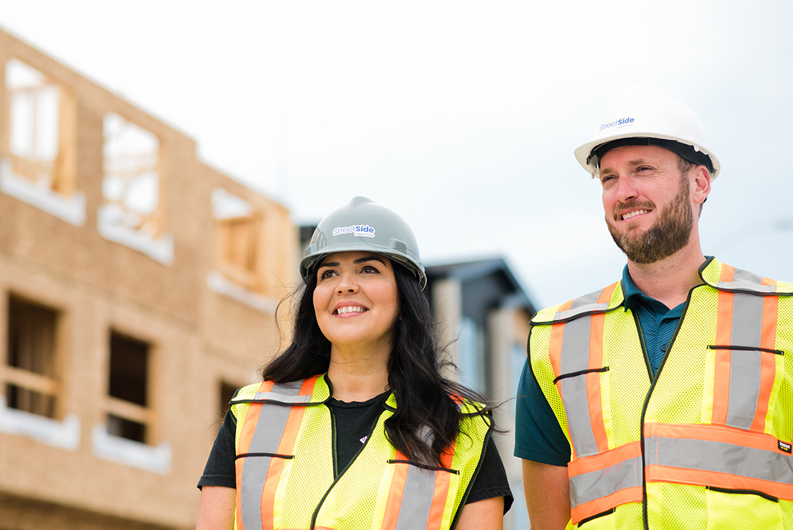 Image of Qualico Streetside developments employees visiting a job site wearing construction hats and reflective vests